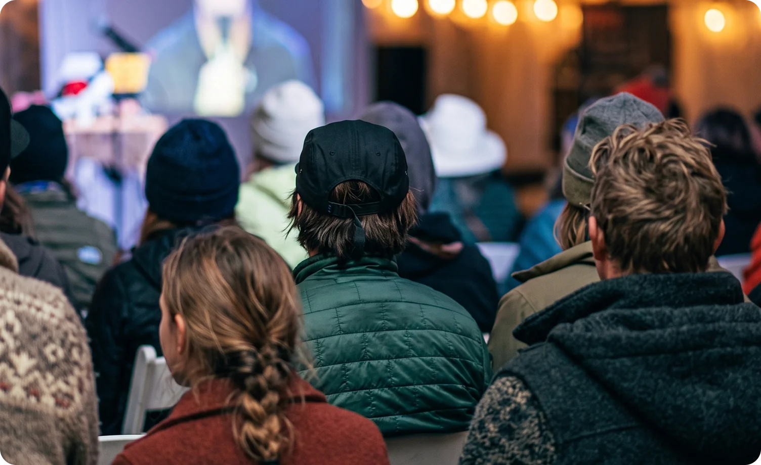 An audience watching a film on a lit screen at an indoor evening screening